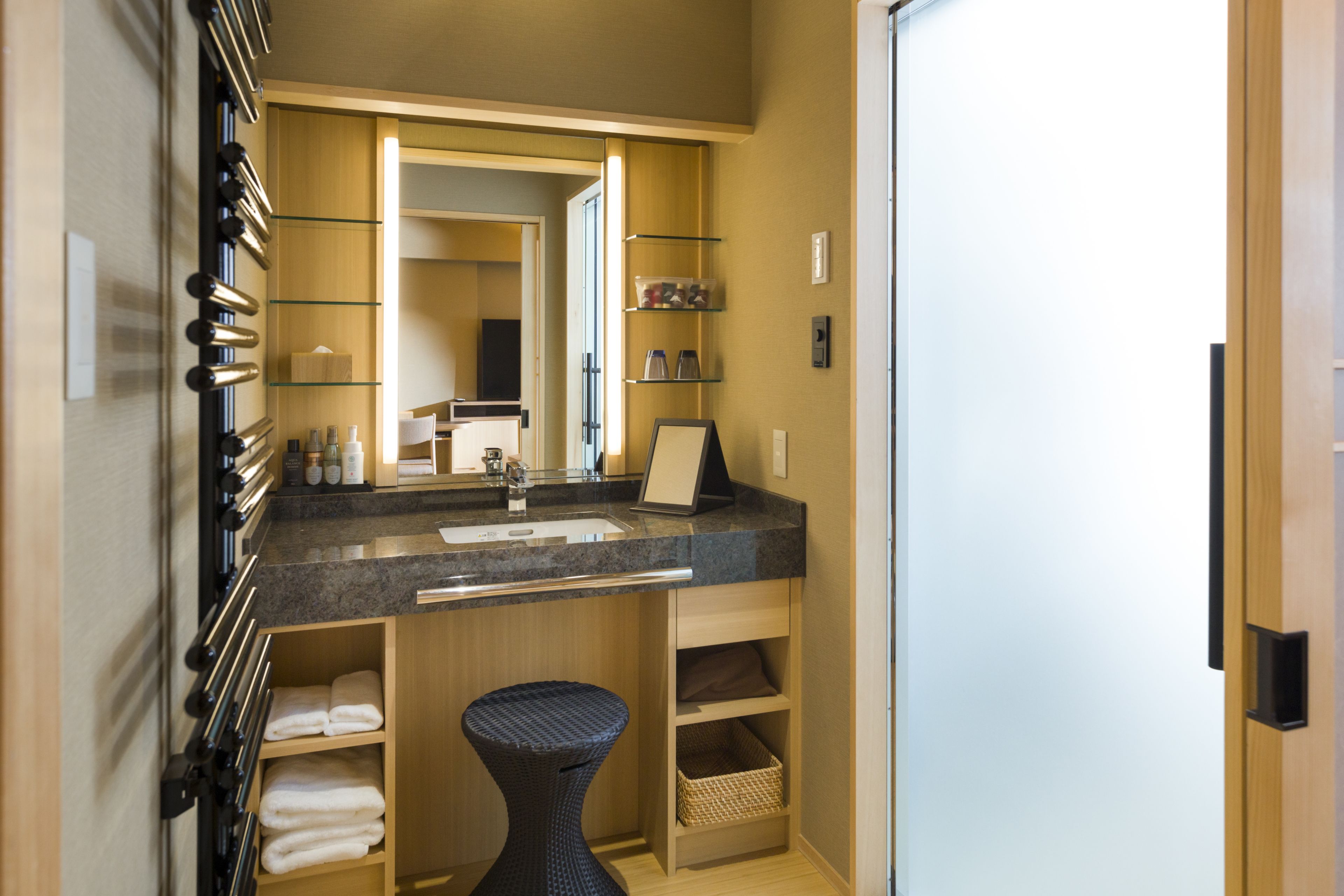 Un baño moderno con encimera de granito, lavabo y espejo. Hay repisas con artículos de aseo y un perchero.