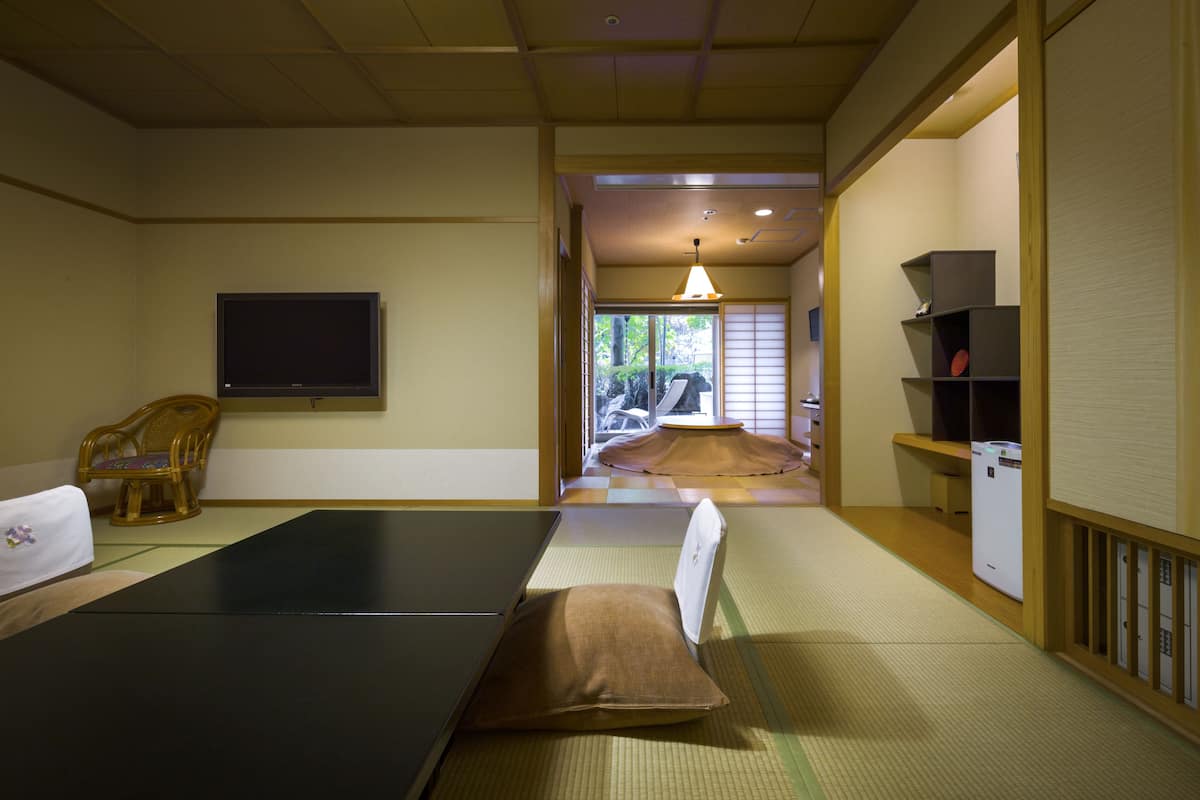 Ein traditioneller japanischer Raum mit Tatami-Bodenbelag, einem Tatami-Tisch, einem Fernseher und einem Futonbett.