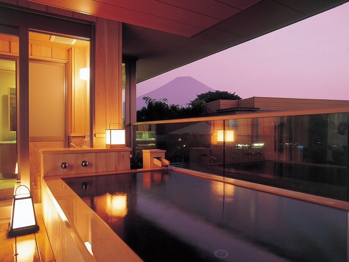 A modern indoor pool area with a glass enclosure, wooden furniture, and a view of a mountain at dusk.