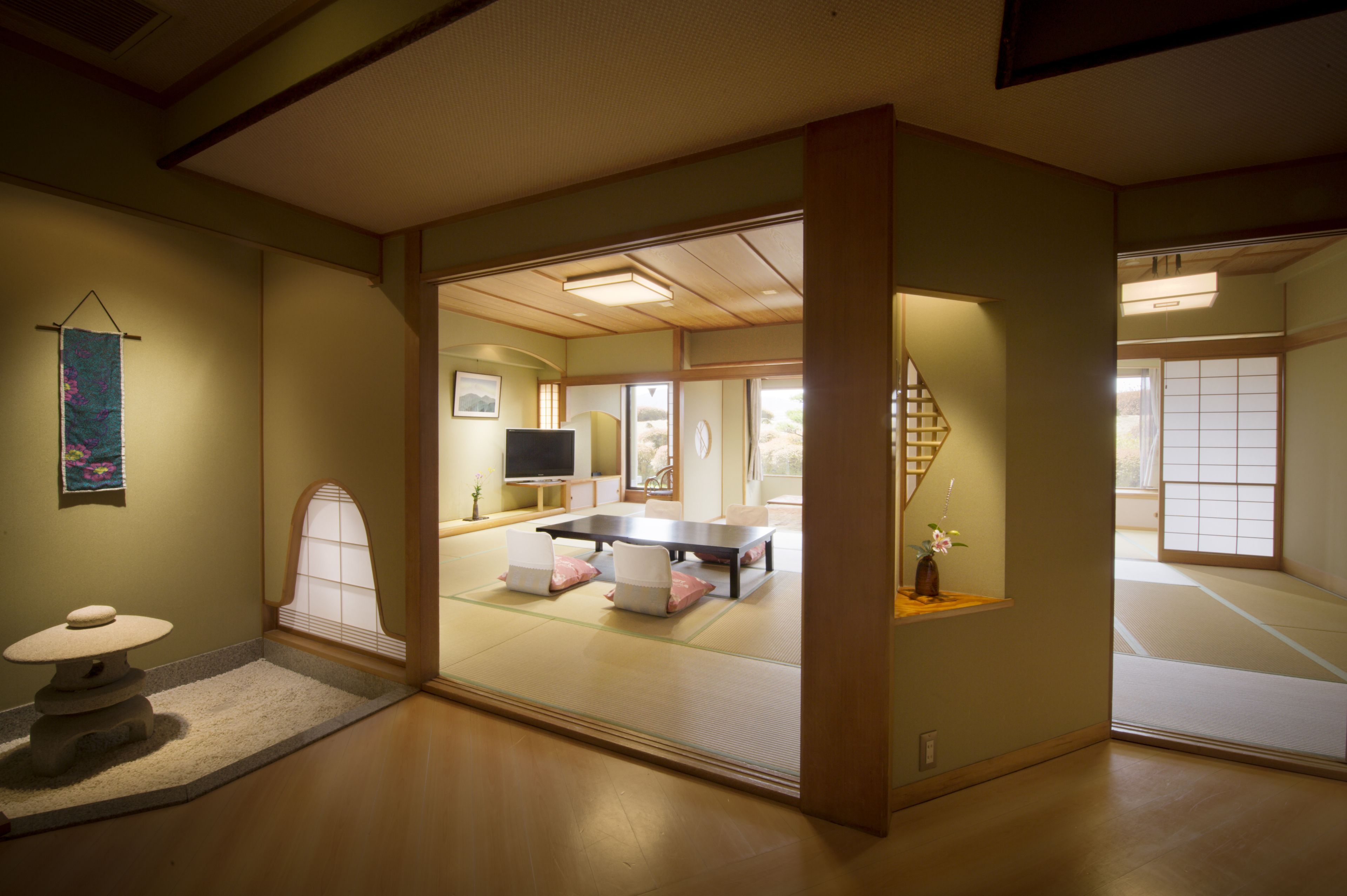 A traditional Japanese room with tatami flooring, a tatami mat table, a low table with a vase, and a television.