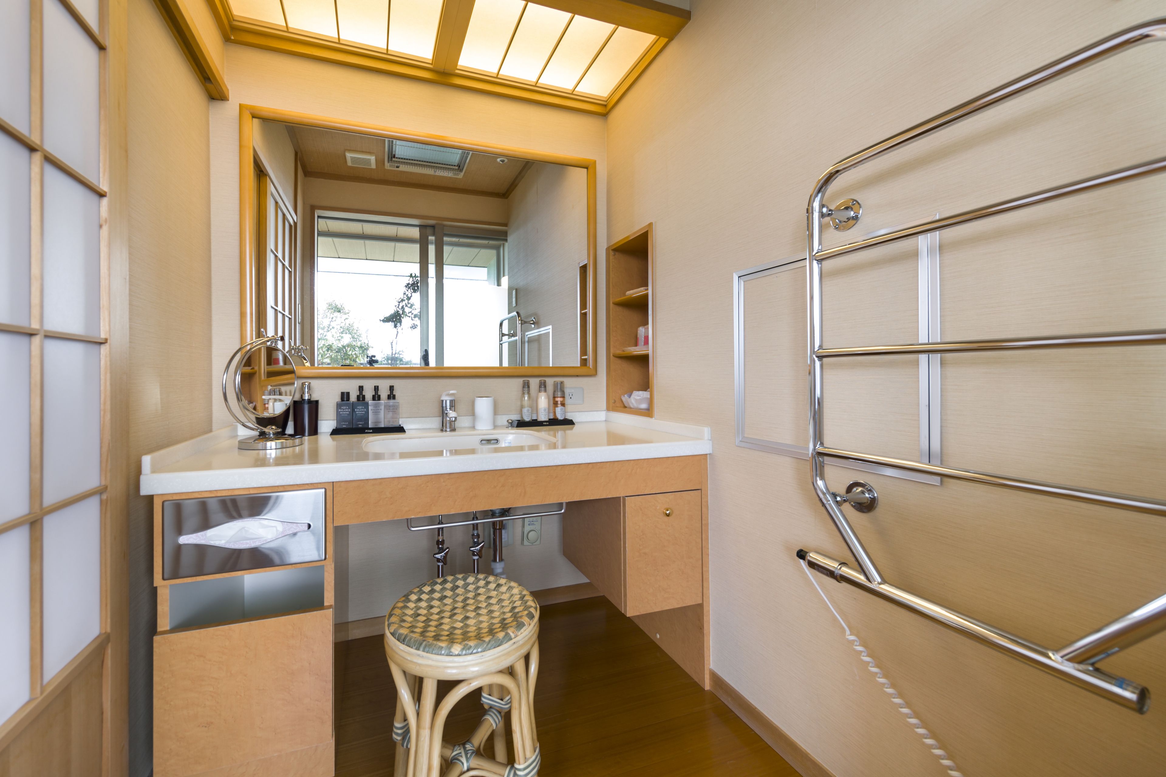 A bathroom with a large mirror, a sink, a stool, and a towel rack.