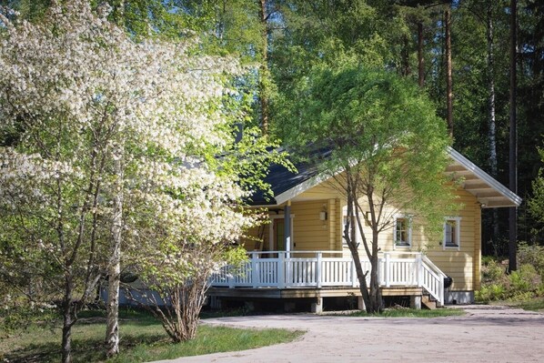 Ett gult hus med en veranda, omgivet av träd och en klar himmel.