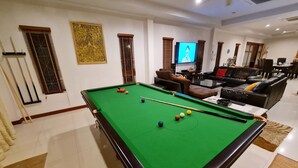 A pool table with balls, a television, and a sofa in a room with white walls and a tiled floor. - Thiva Pool Villa Hua Hin (Hua Hin)