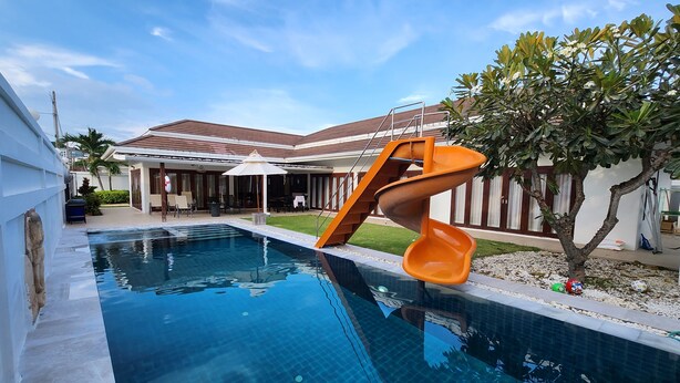 A swimming pool with a slide, a covered patio, and a house with a tiled roof. - Thiva Pool Villa Hua Hin (Hua Hin)