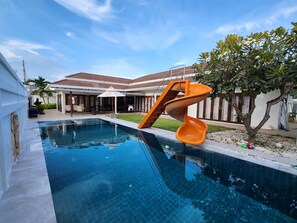 Una piscina con tobogán, un porche cubierto y una casa con techo de tejas.