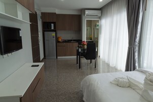 A modern hotel room with a bed, a desk, a kitchenette, and a bathroom.