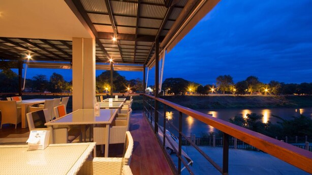 An outdoor dining area with tables and chairs, overlooking a body of water at dusk. - Dragon River Avenue Hotel (Phitsanulok)