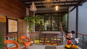 A modern lobby with a staircase, orange chairs, a large plant, and a Mickey Mouse statue. - Dragon River Avenue Hotel (Phitsanulok)