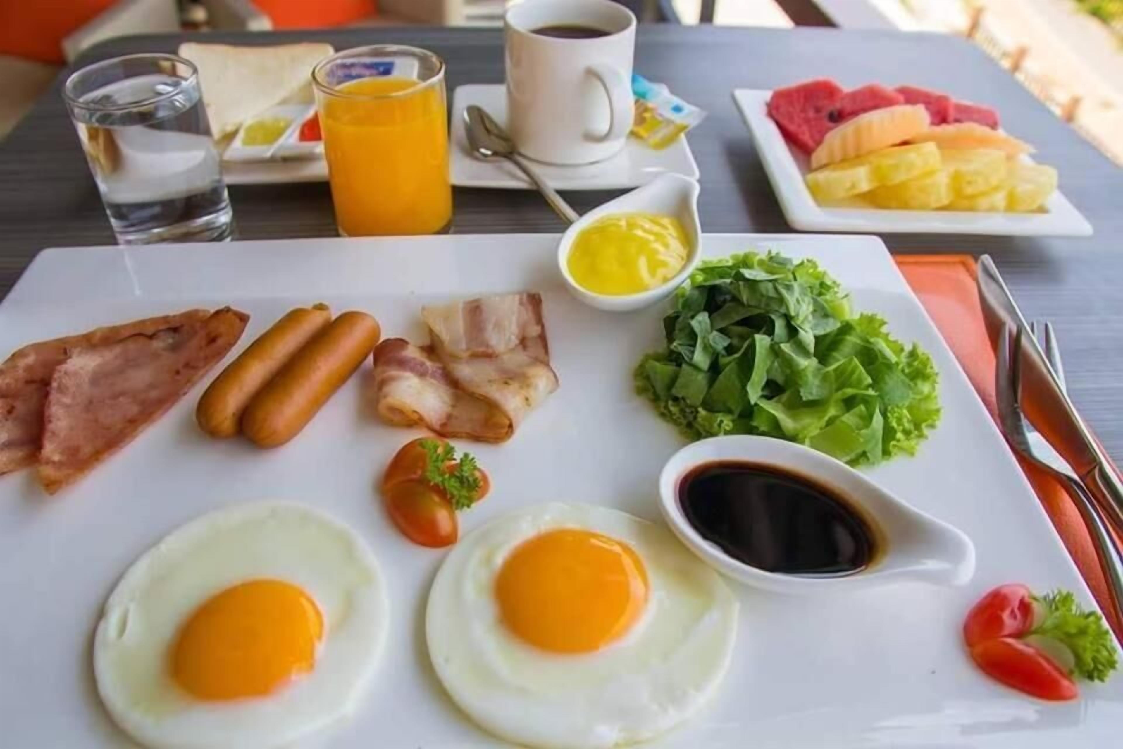 A breakfast plate with eggs, bacon, sausages, and toast, accompanied by a cup of coffee, a glass of water, and a plate of fruit.