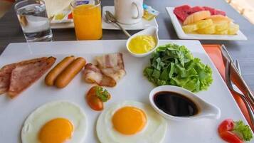 A breakfast plate with eggs, bacon, sausages, and toast, accompanied by a cup of coffee, a glass of water, and a plate of fruit.