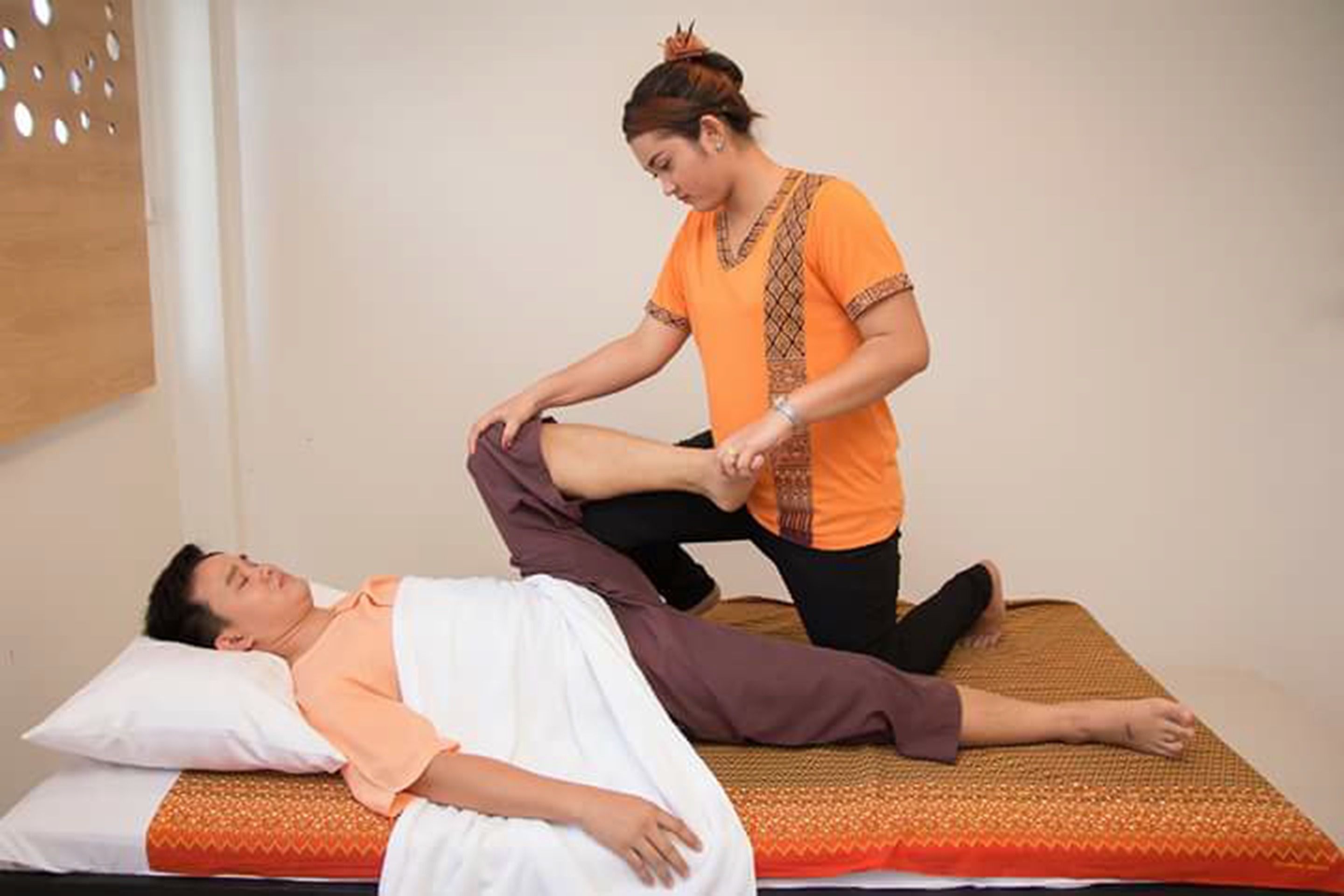 A massage therapy session in a room with a bed, a massage table, and a plain wall.