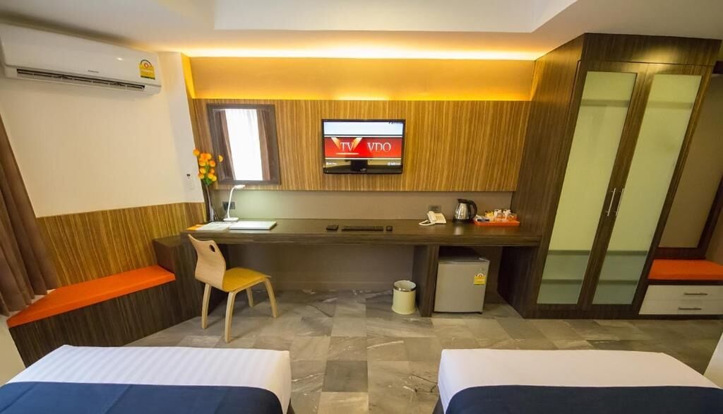 A hotel room with two beds, a desk with a TV, a small fridge, and a wardrobe.