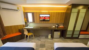 A hotel room with two beds, a desk with a TV, a small fridge, and a wardrobe.