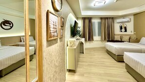A hotel room with two beds, a large mirror, a clock, a television, and a desk with a plant. - Dragon River Avenue Hotel (Phitsanulok)