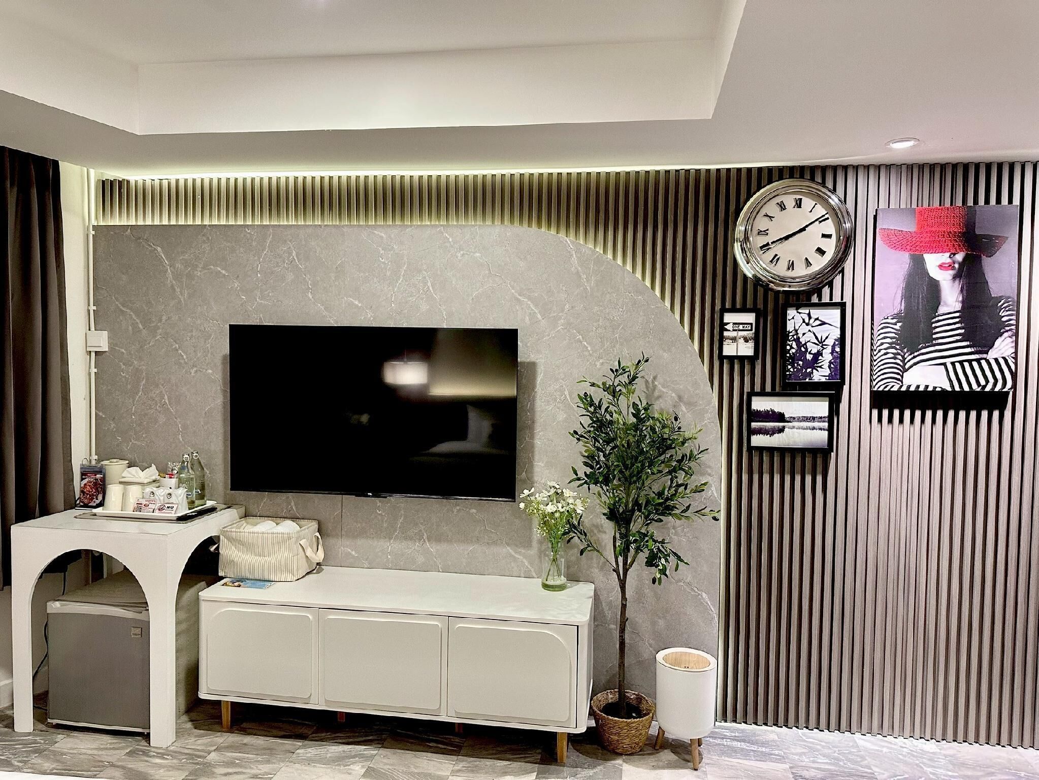 A modern living room with a flat-screen TV, a white console, a potted plant, and a clock on the wall.
