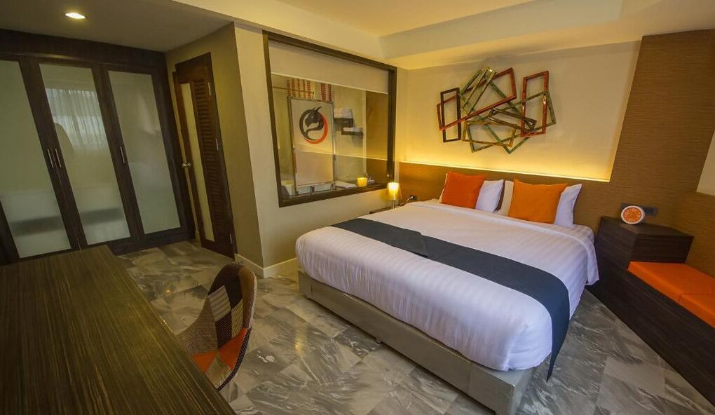 A hotel room with a large bed, a desk, and a chair. There is a mirror on the wall and a clock on the nightstand.