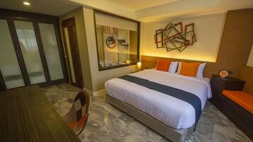 A hotel room with a large bed, a desk, and a chair. There is a mirror on the wall and a clock on the nightstand.