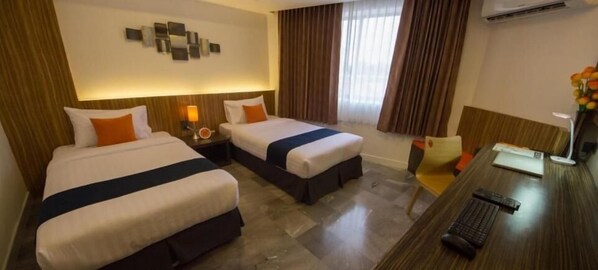 A hotel room with two beds, a desk with a computer, a chair, and a decorative wall piece.