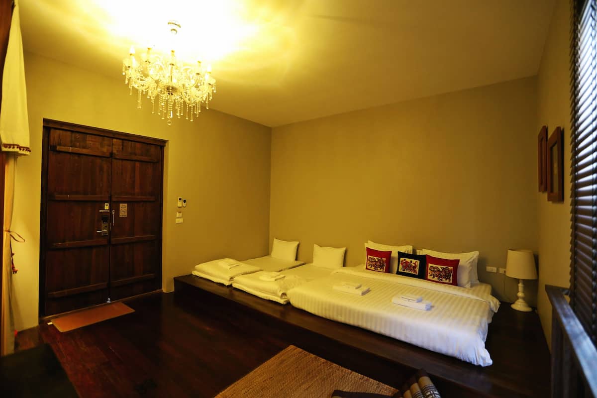 A hotel room with a large bed, a chandelier, wooden wardrobe, and a bedside table with a lamp.