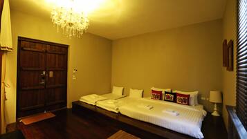 A hotel room with a large bed, a chandelier, wooden wardrobe, and a bedside table with a lamp.