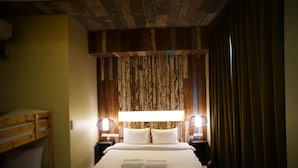 A hotel room with a bunk bed, a large bed with white linens, two bedside lamps, and a wooden headboard.