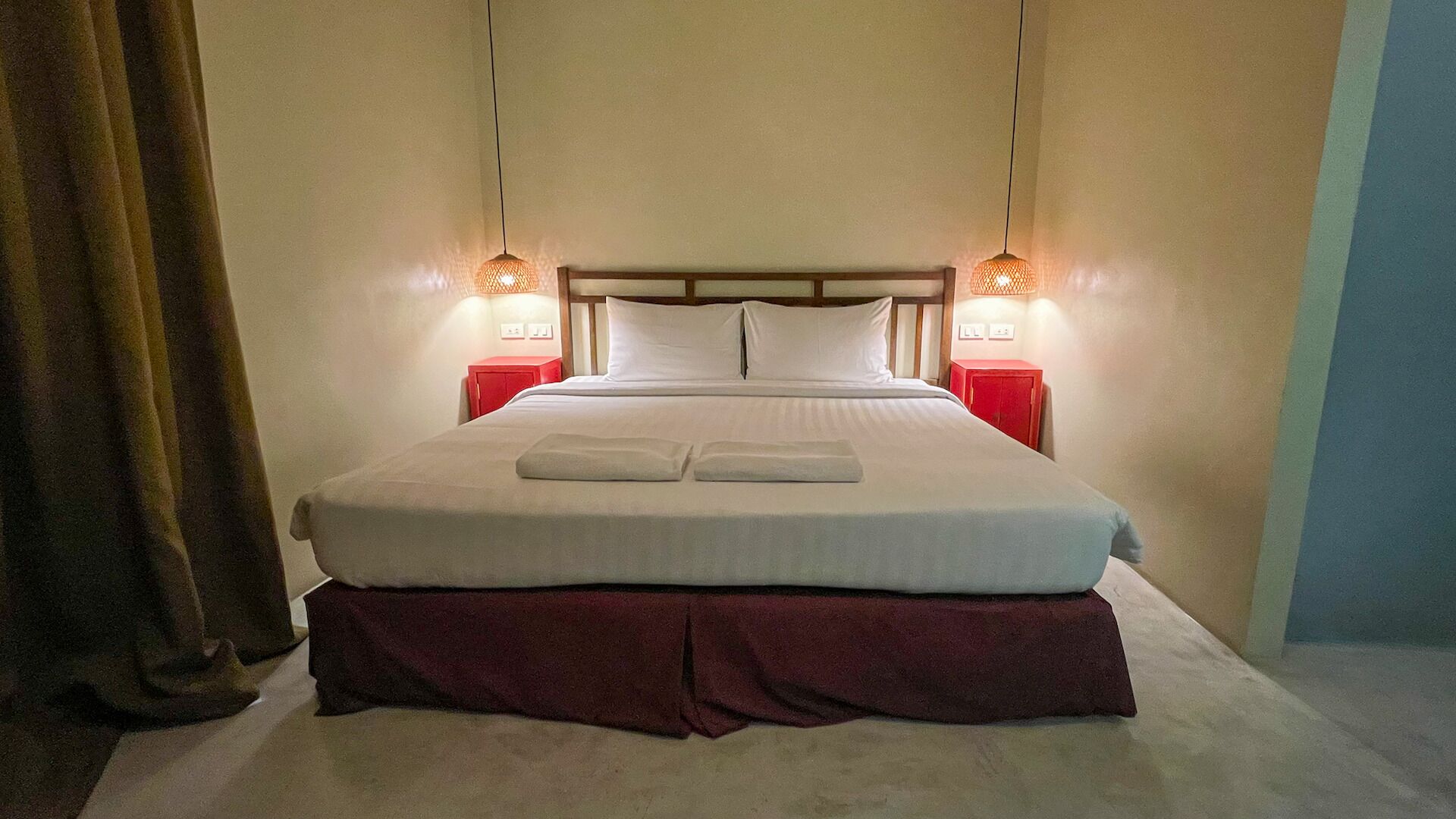 A neatly made bed with two pillows, a red nightstand, and two wall-mounted lamps.