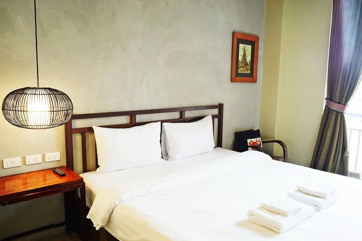 A hotel room with a neatly made bed, a bedside table with a remote control, a hanging light fixture, and a framed picture on the wall.