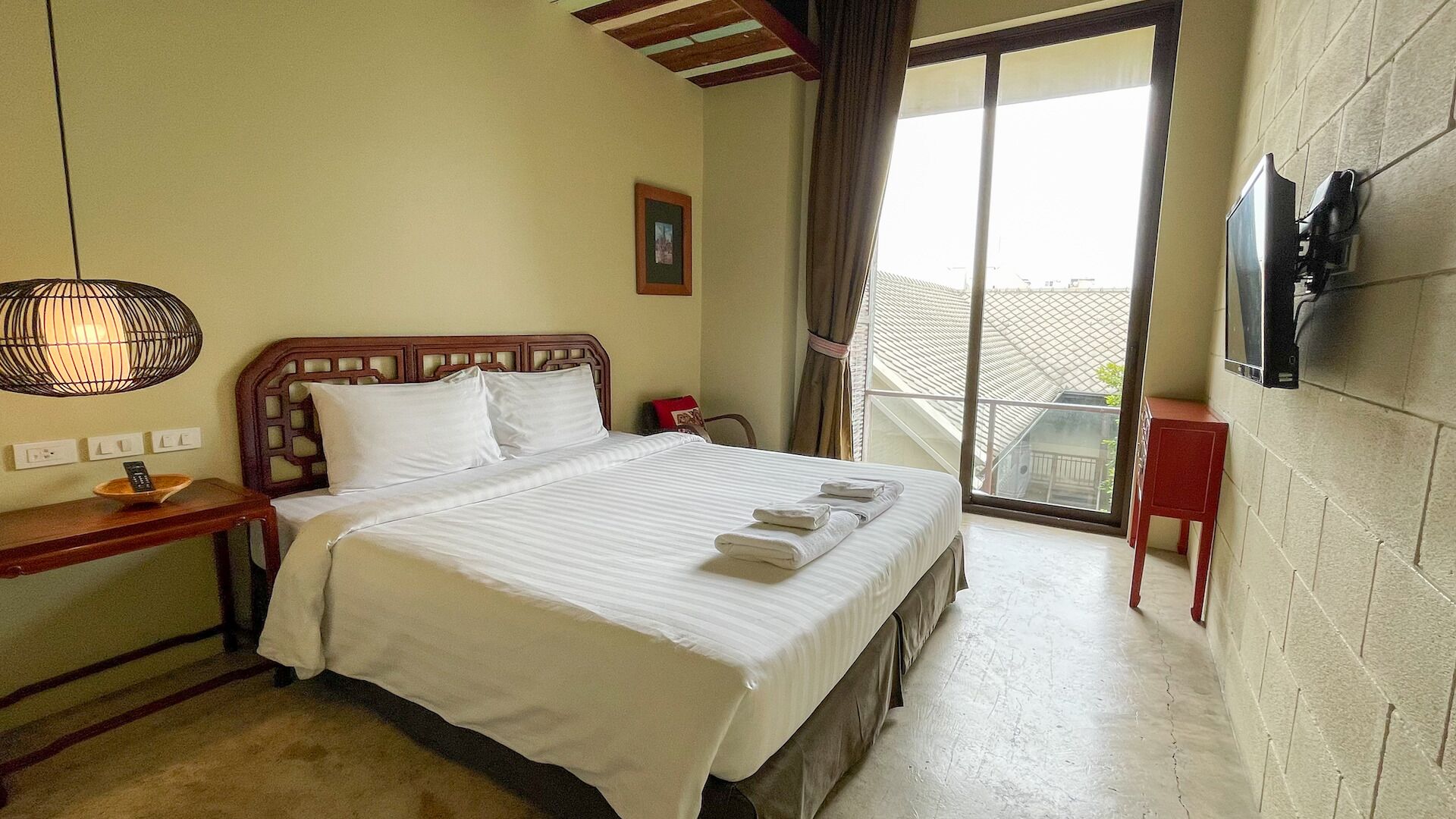 A hotel room with a bed, a bedside table with a lamp, a TV mounted on the wall, and a view of the outside balcony.