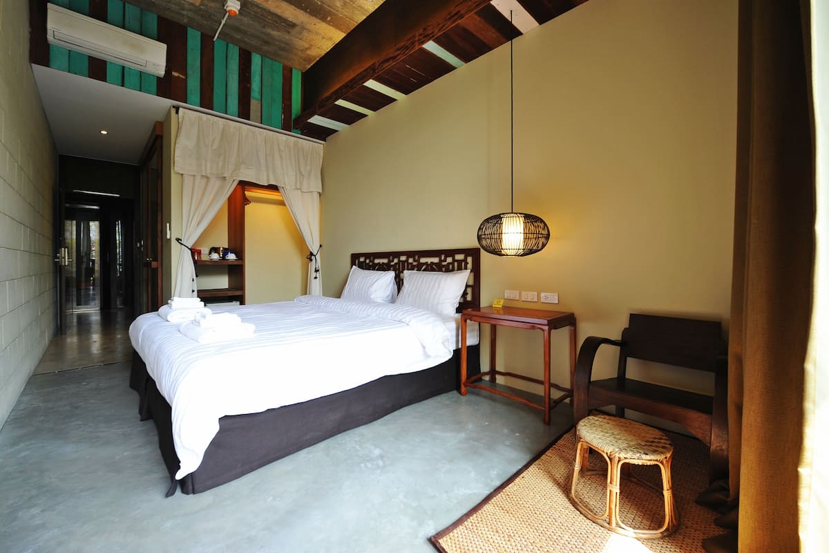 A hotel room with a large bed, a small table, a chair, and a hanging light fixture.