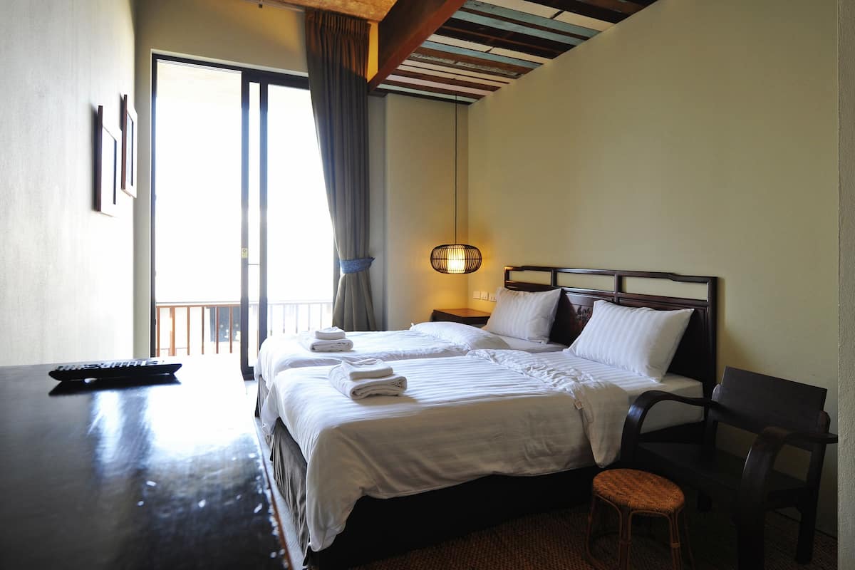 A hotel room with two beds, a desk, a chair, a lamp, and a window with curtains.