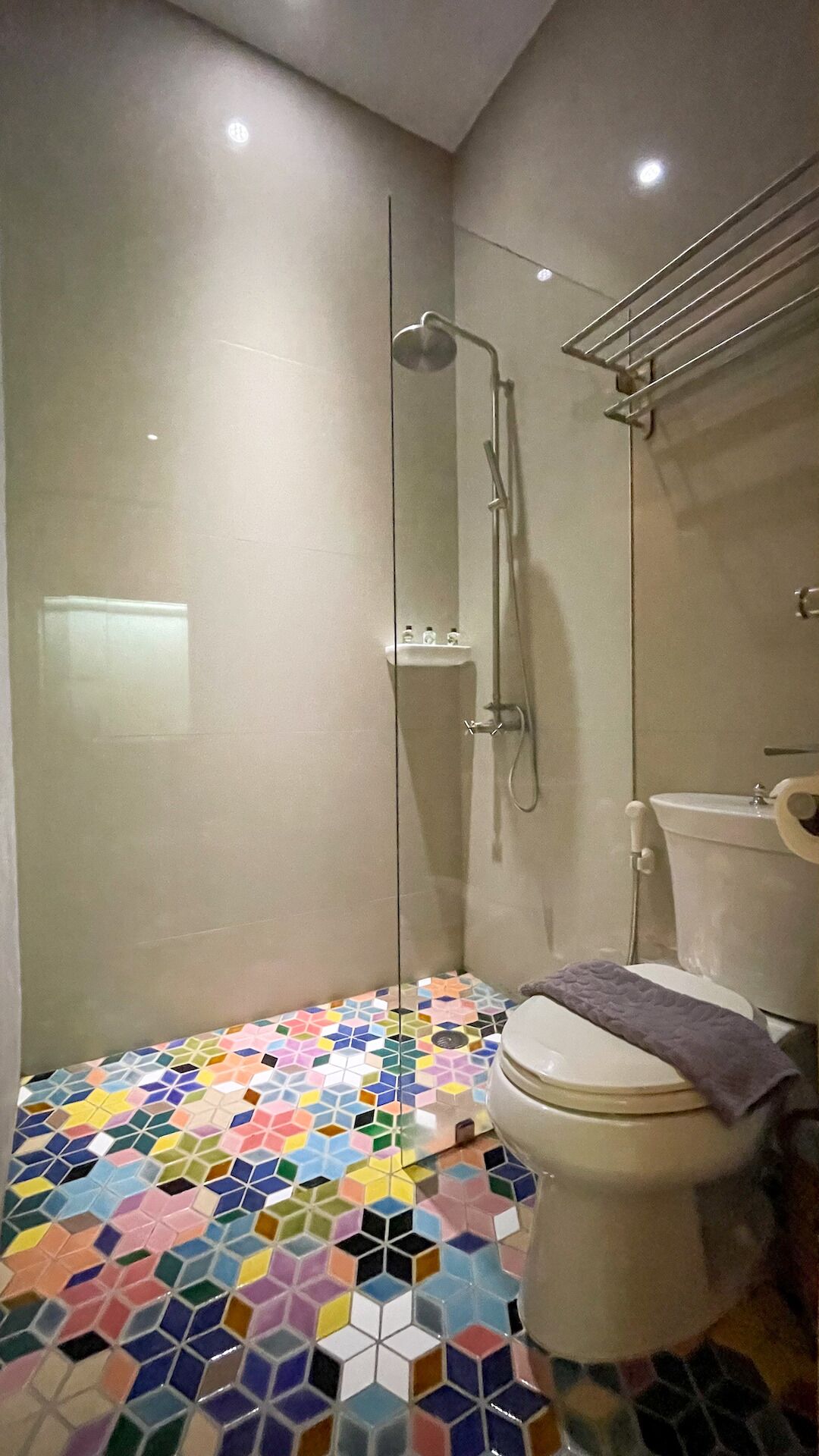 A bathroom with a shower, toilet, and a colorful hexagonal tile floor.