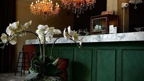A reception area with a marble counter, two chandeliers, white orchids, and a green wall.