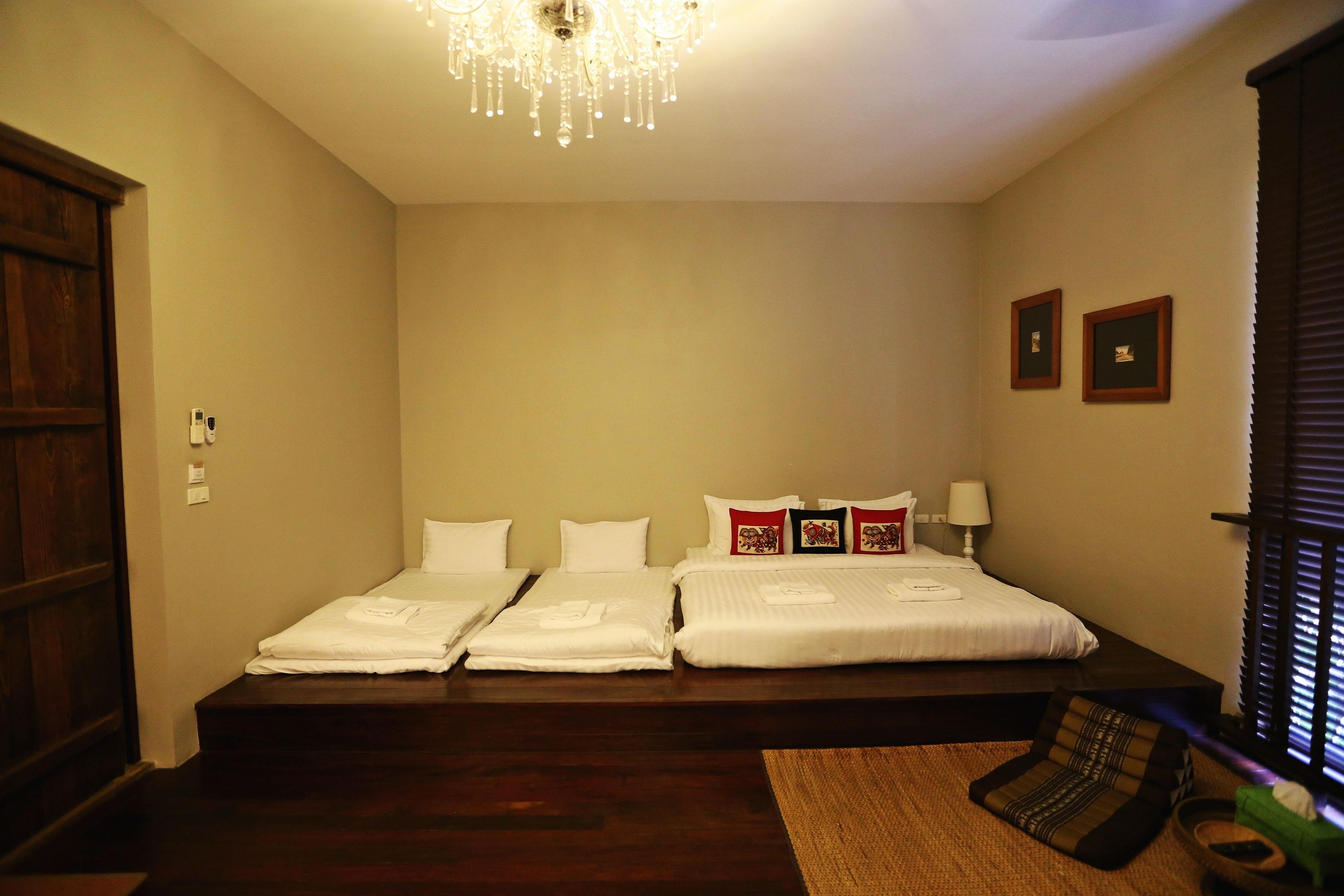 A hotel room with three beds, a chandelier, a wooden floor, and a window with blinds.