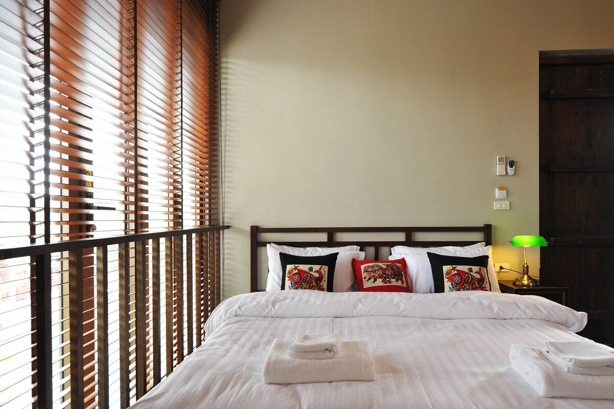 A neatly made bed with white linens and towels, a wooden headboard, and decorative pillows.