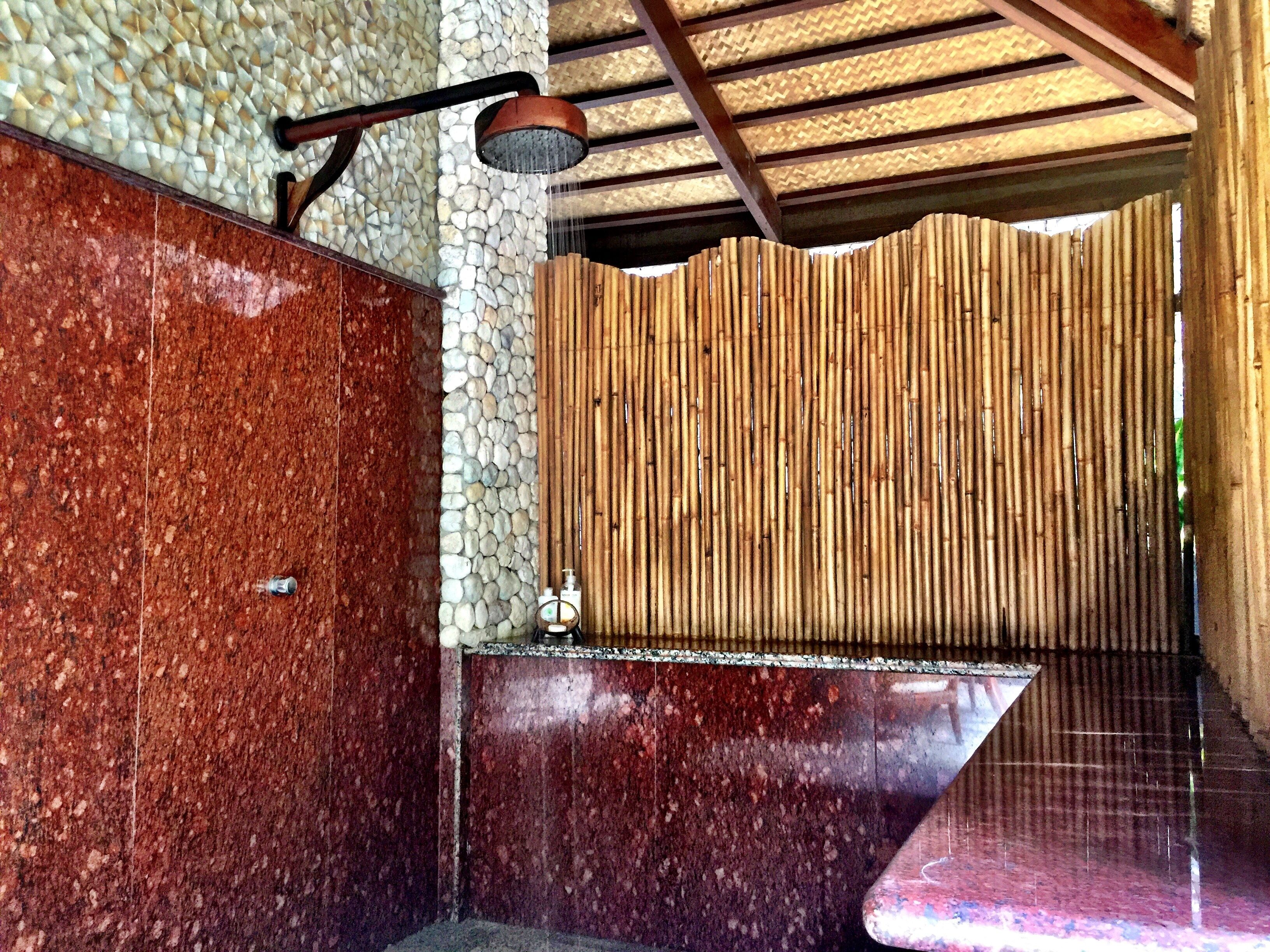 A bathroom with a stone wall, a bamboo partition, and a shower area.