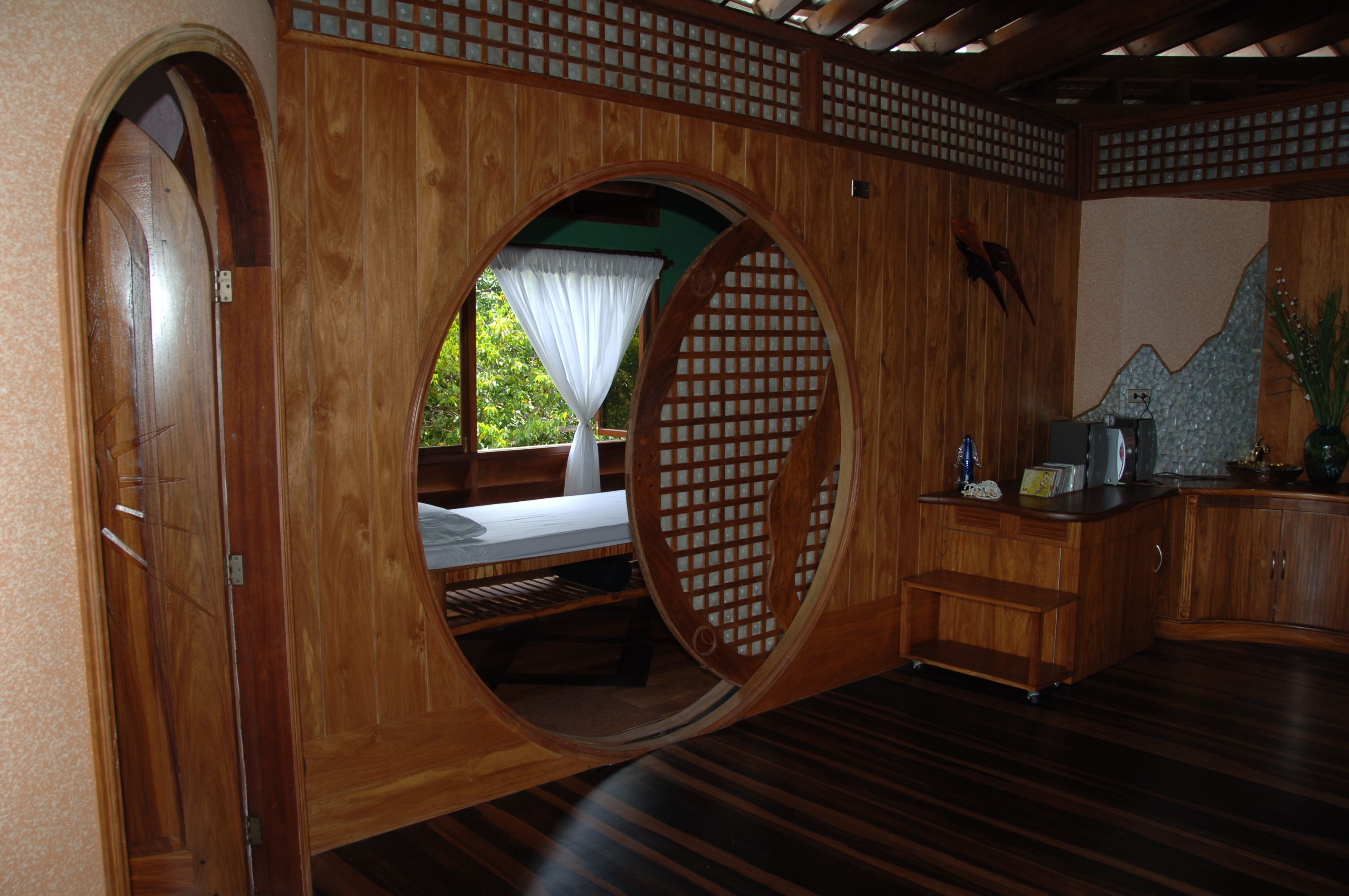 Una habitación con detalles de madera, una cama con dosel blanco, un escritorio pequeño y vistas a la vegetación exterior.