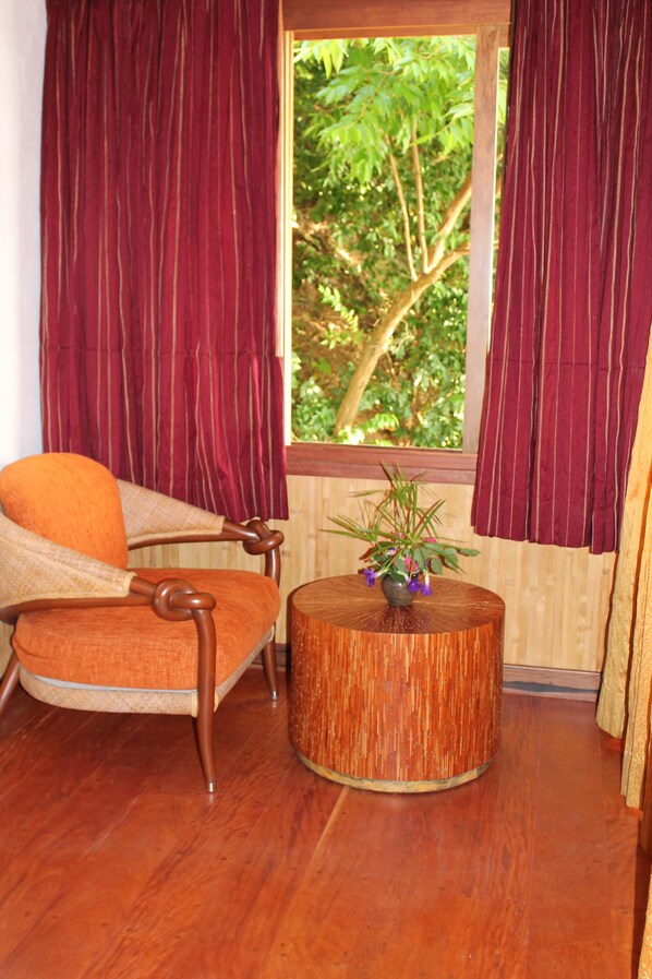 A room with a wooden chair, a round wooden table with a potted plant, and a window with red curtains.
