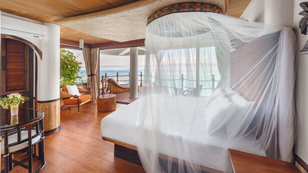 Een luxueuze slaapkamer met hemelbed, houten vloeren en uitzicht op zee.