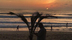 A beach scene with palm trees and people in the water during sunset. - Holiday Home Patong (Patong)