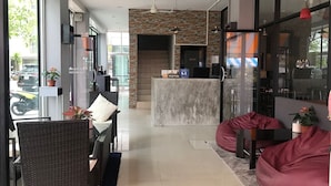 A modern reception area with a stone wall, a reception desk, and seating arrangements including wicker chairs and bean bags. - Holiday Home Patong (Patong)