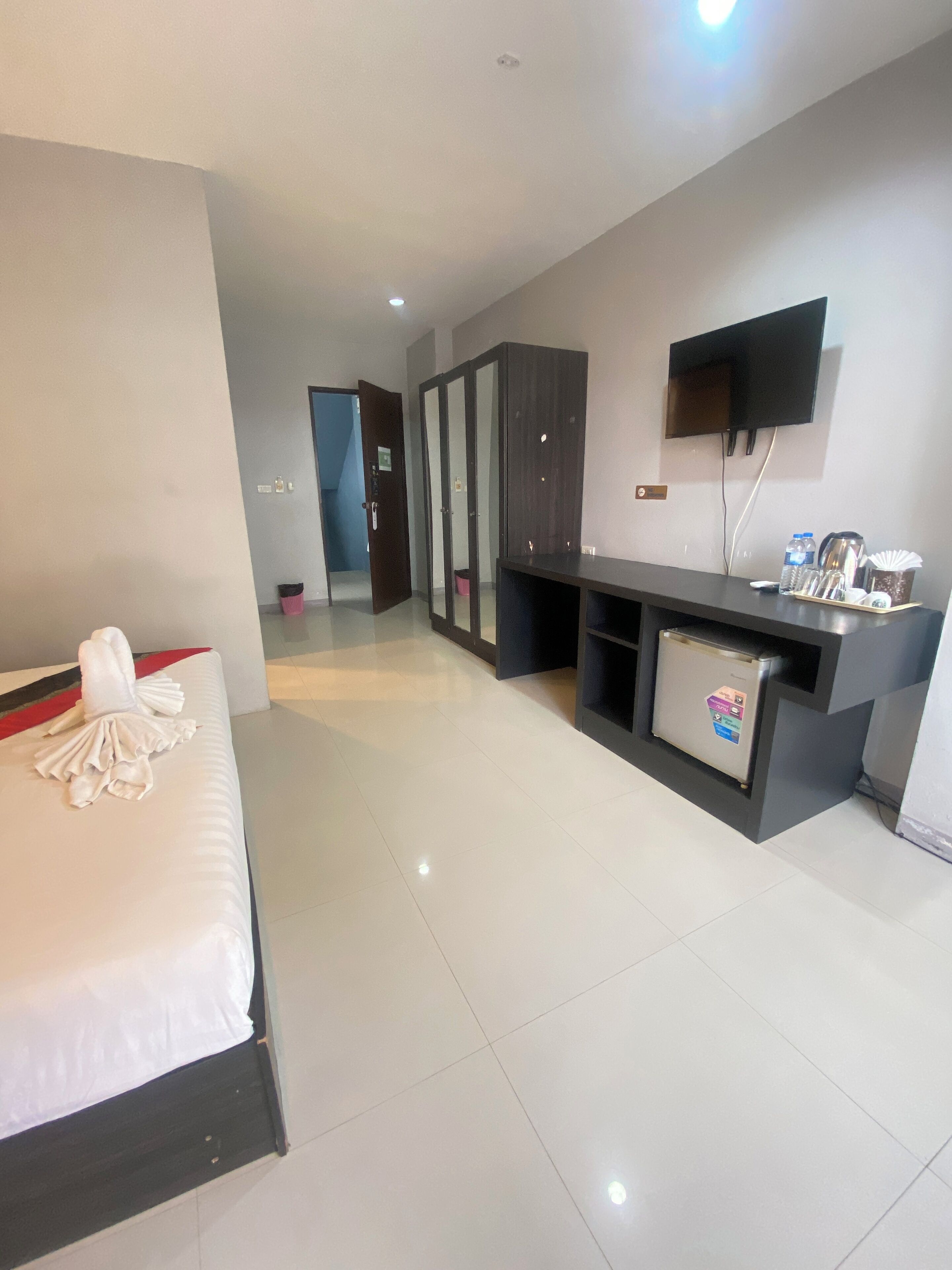 A hotel room with a bed, a desk with a flat-screen TV, a minibar, and a wardrobe.