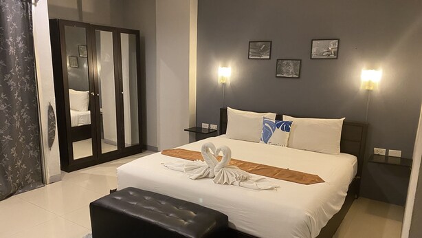 A hotel room with a bed, a black ottoman, a mirror, and wall-mounted lights. - Holiday Home Patong (Patong)