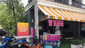 A travel information booth with a signboard for 'Holiday Home' and a motorcycle parked in front. - Holiday Home Patong (Patong)