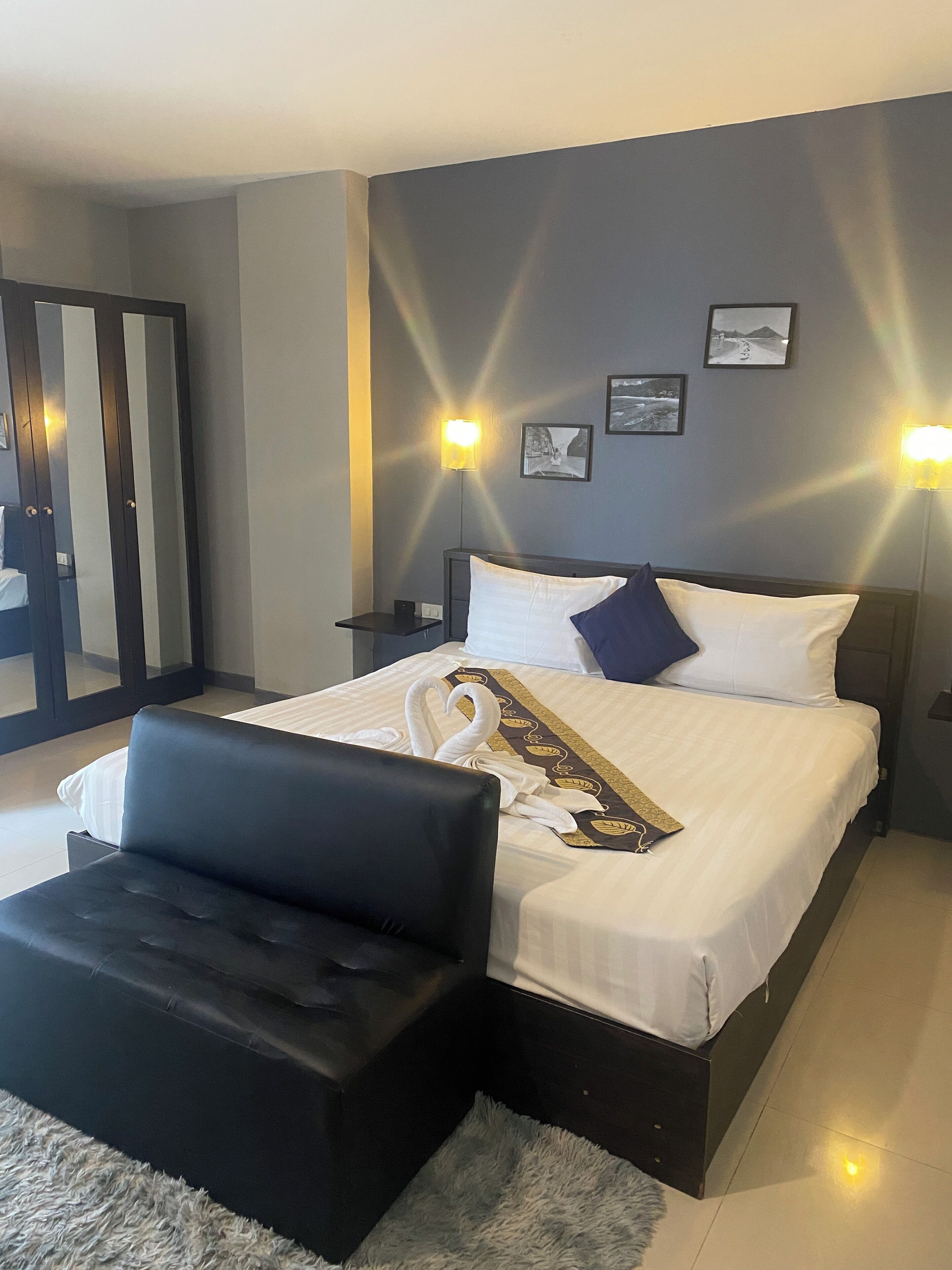 A hotel room with a large bed, a black ottoman, and a mirror with a sliding door.