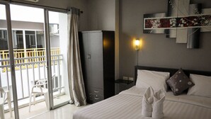 A hotel room with a bed, a wardrobe, a nightstand, a wall-mounted light, and a view of the outside balcony. - Holiday Home Patong (Patong)