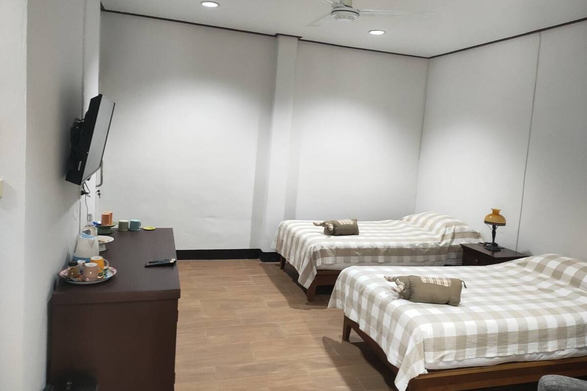 A hotel room with two beds, a desk, a television, and a ceiling fan.