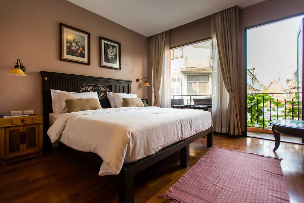 A bedroom with a large bed, a nightstand, a lamp, and a view of the outside balcony.