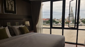 Ein Hotelzimmer mit einem großen Bett, einem Fenster mit Blick auf einen Fluss und Gebäude sowie einem gerahmten Bild an der Wand.
