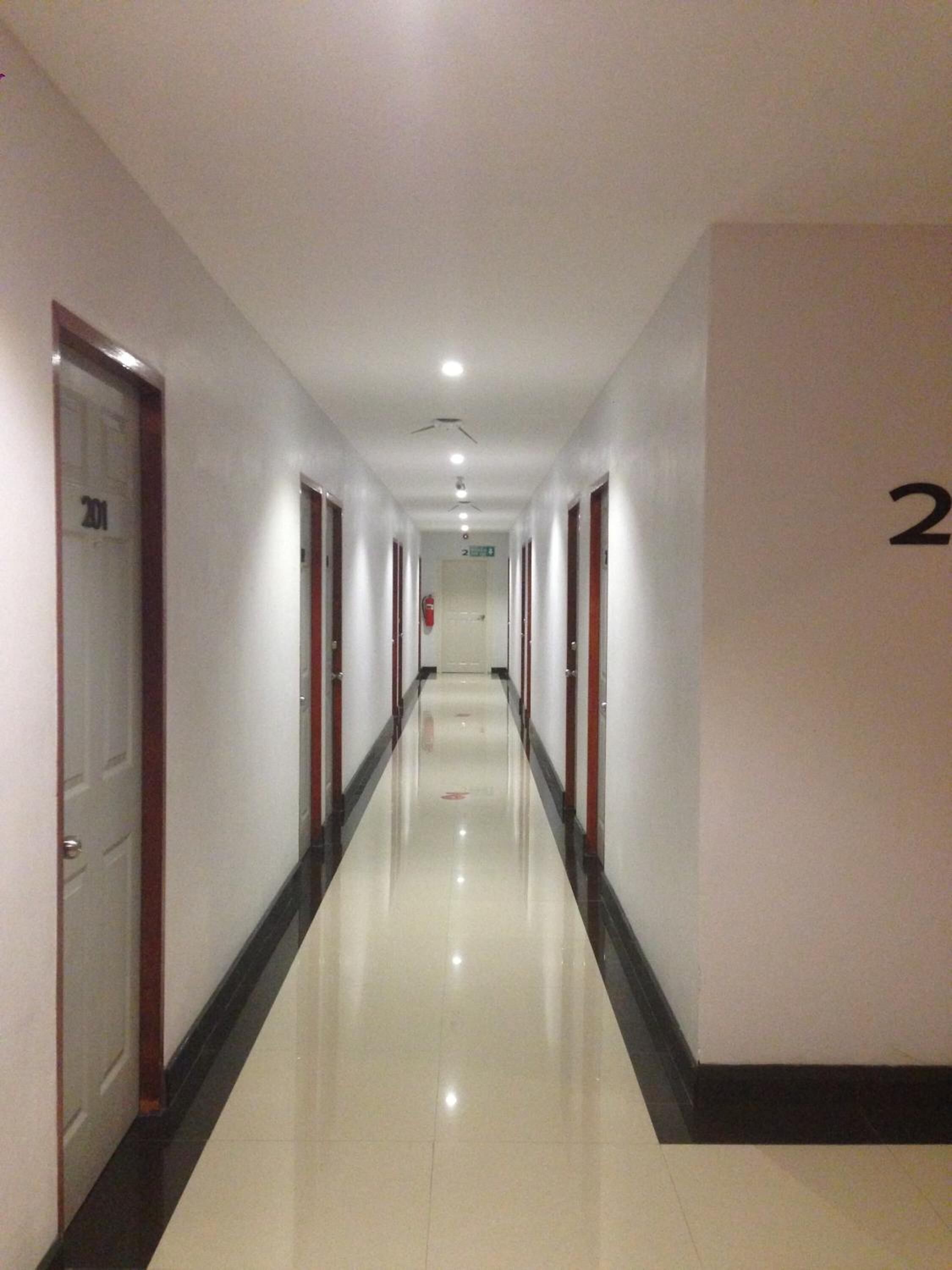 En lang, smal hotelgang med døre på begge sider, et skinnende flisegulv og et loft med indbyggede lys.