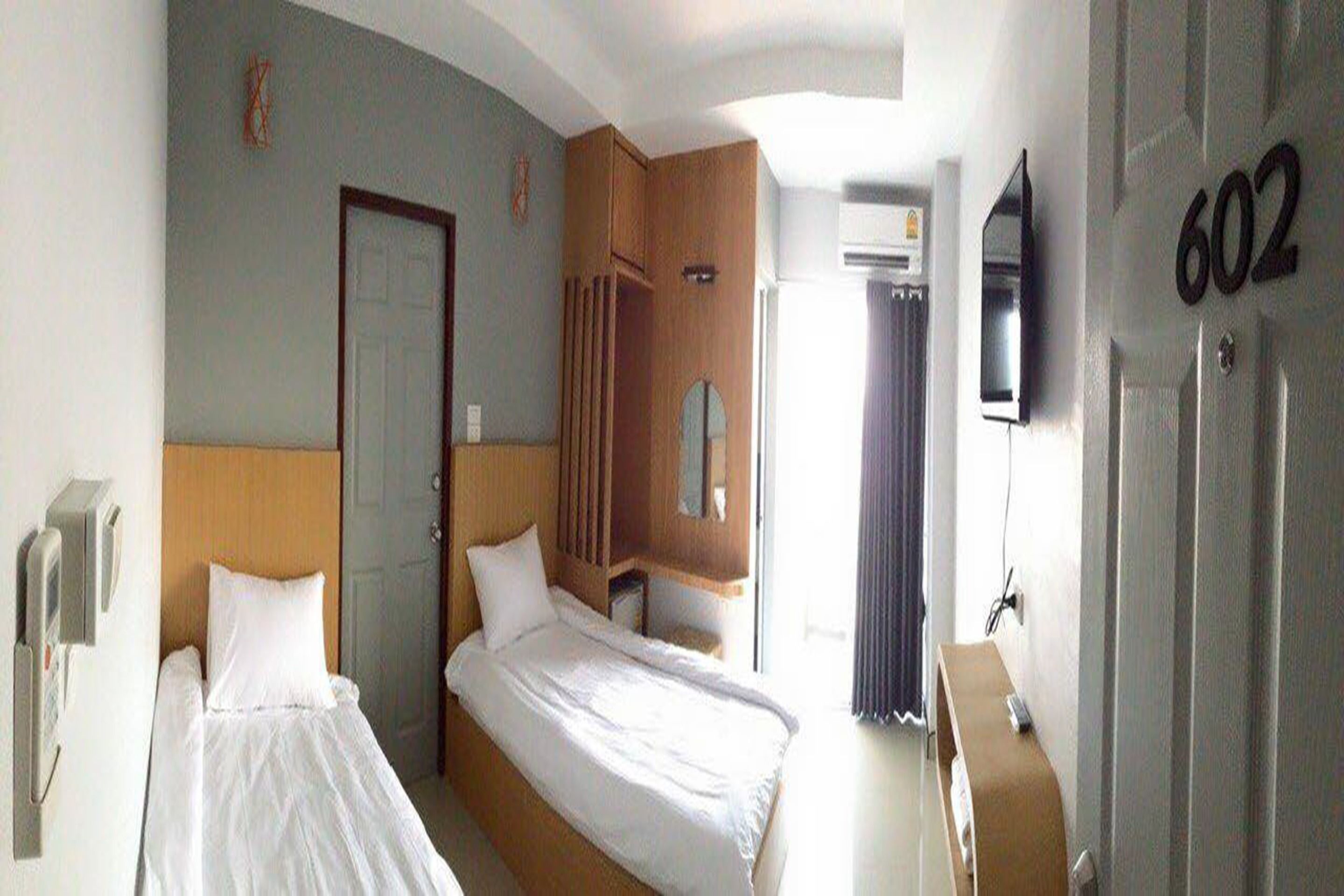 A hotel room with two beds, a wooden wardrobe, a mirror, a TV, and a number '602' on the wall.